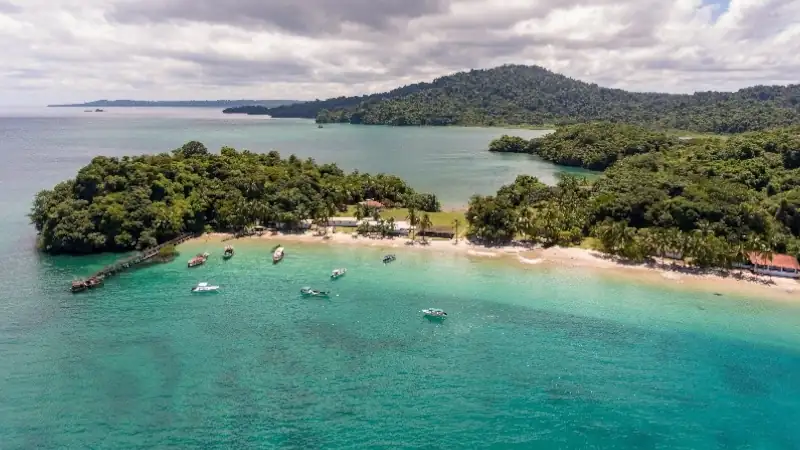 Aerial view of a tropical beach in Panama, surrounded by turquoise Caribbean waters, lush rainforest, and forested islands.