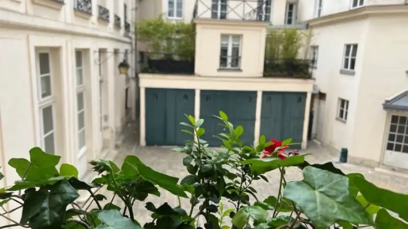 Quiet Paris-style apartment courtyard with cream-colored buildings, green plants, and private garage doors viewed from a balcony.