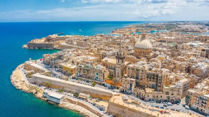 Aerial view of Valletta, Malta, showcasing the historic waterfront, fortified walls, and the city's iconic domed skyline along the Mediterranean Sea.
