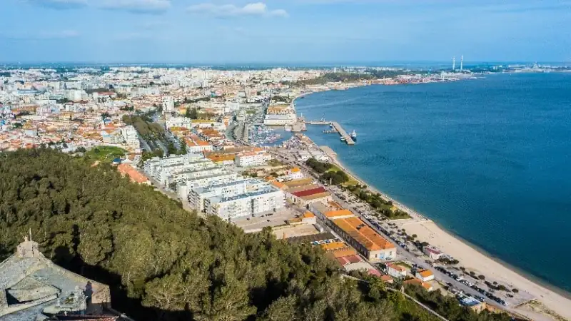 A panoramic aerial view of a coastal city with a sandy beach, marina, waterfront promenade, and expansive bay.