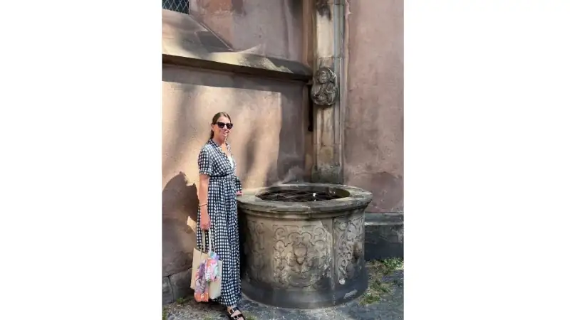 Kathleen standing beside a historic stone well in Strasbourg, France, wearing a black-and-white checkered dress.