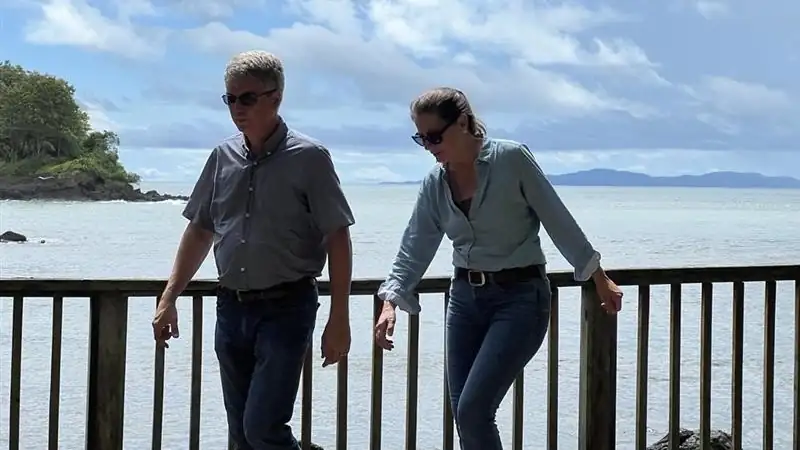 Kathleen and Lief walking along a seaside boardwalk with ocean views and cloudy skies in the background.
