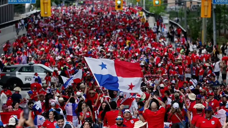 Thousands of Panama soccer fans dressed in red march through a city street waving Panamanian flags and celebrating their national team.