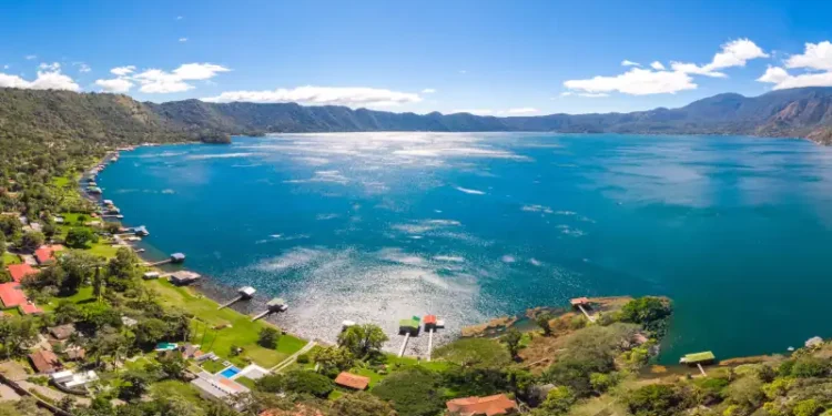 Panoramic view of the beautiful lake of Coatepeque in El Salvador, with a blue sky, in the season where its waters are turquoise and most of its mountains and vegetation are green.