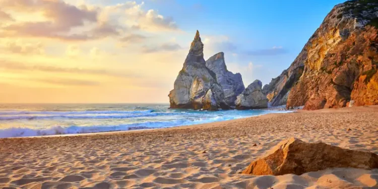 Portugal Ursa Beach at atlantic coast of Atlantic Ocean with rocks and sunset sun waves and foam at sand of coastline picturesque landscape panorama.