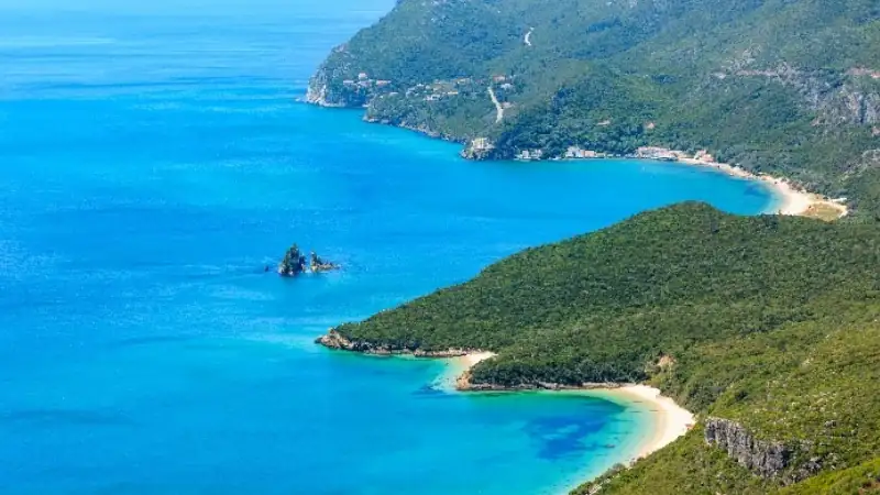 A stunning coastal landscape featuring turquoise waters, secluded sandy coves, and lush green hills along the shoreline.
