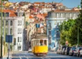 conic yellow Tram 28 on a historic cobblestone street in Lisbon, Portugal, with colorful European architecture in the background.