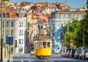 conic yellow Tram 28 on a historic cobblestone street in Lisbon, Portugal, with colorful European architecture in the background.