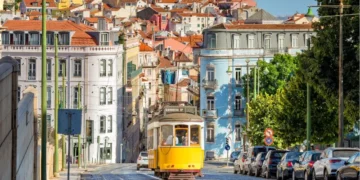 conic yellow Tram 28 on a historic cobblestone street in Lisbon, Portugal, with colorful European architecture in the background.