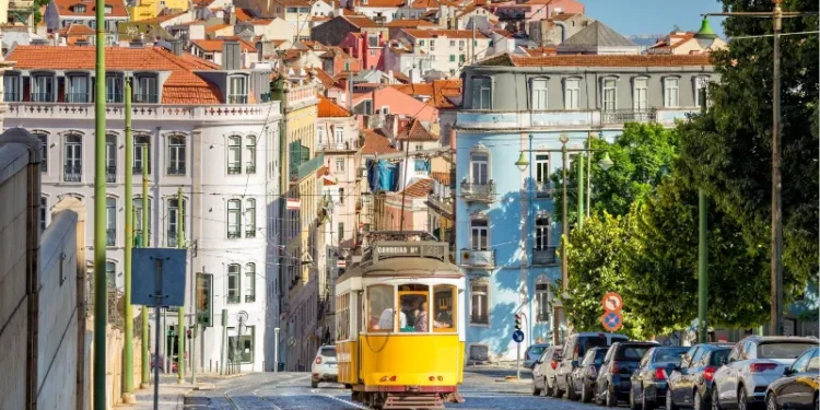 conic yellow Tram 28 on a historic cobblestone street in Lisbon, Portugal, with colorful European architecture in the background.