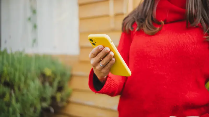 Anonymous young woman using her smartphone in her home garden, enjoying a peaceful outdoor moment while staying connected through mobile technology.