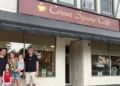 A family stands outside Corner Square Cafe, posing together in front of the café entrance on a small-town main street.