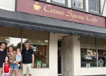 A family stands outside Corner Square Cafe, posing together in front of the café entrance on a small-town main street.