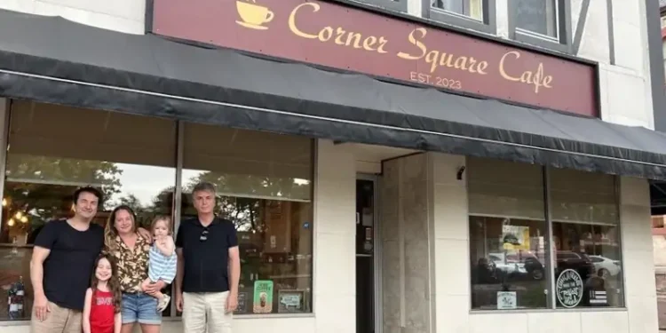 A family stands outside Corner Square Cafe, posing together in front of the café entrance on a small-town main street.