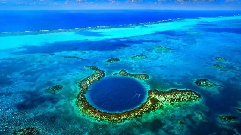 An aerial view of the Great Blue Hole in Belize, featuring the iconic circular marine sinkhole surrounded by vibrant turquoise coral reefs in the Caribbean Sea.