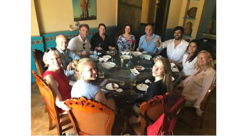 Lief and Kathleen enjoy a shared meal with other people around a large dining table in a warm, elegant restaurant setting.