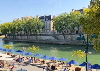 Locals gathered under blue umbrellas. Beach on Seine river in the center of Paris