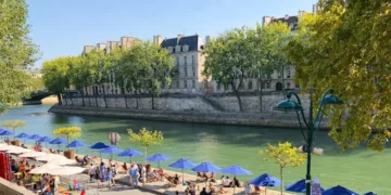 Locals gathered under blue umbrellas. Beach on Seine river in the center of Paris
