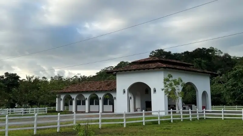 Elegant equestrian ranch featuring Spanish-style architecture, white fencing, and a peaceful natural landscape.