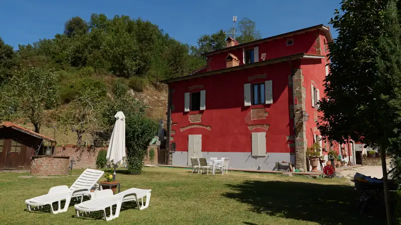 A red house, mansion in the valley with chaise lounges on the garden in Tuscany region in Italy