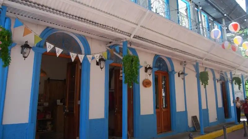 A vibrant colonial street in Panama featuring blue-and-white architecture, ornate ironwork, colorful decorations, and charming local storefronts.