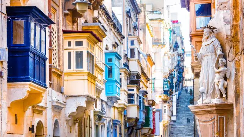 Traditional narrow street with colorful wooden closed balconies in Valletta, Malta. Iconic Maltese architecture in the historic capital district.