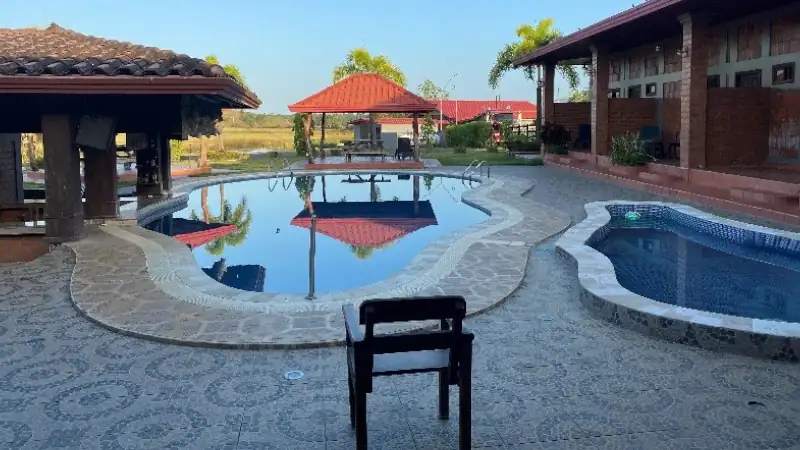 Tropical pool area with stone patios, red-tiled roofs, and lush surroundings.