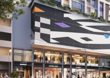 Modern mixed-use building with vibrant street-level retail, including a market, coffee shop, and laundry, featuring a bold geometric mural across the facade.