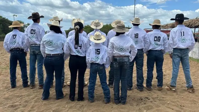 A group of young riders in matching ranch shirts and cowboy hats standing together at an outdoor arena.