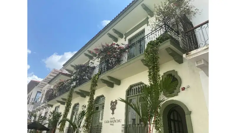 Colonial-style building with ornate iron balconies, lush flowering vines, and tropical plants under a bright blue sky.