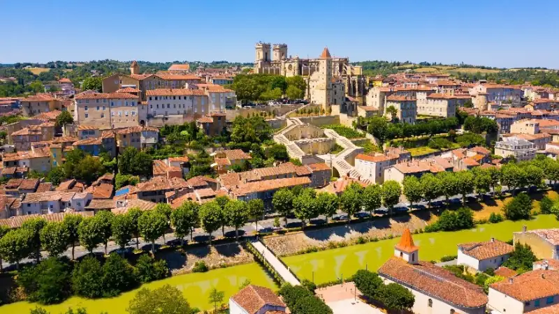 Aerial view of a historic town in Gascony, France, featuring medieval architecture, red-tiled rooftops, and a tree-lined river.