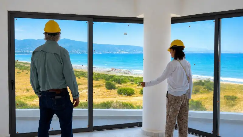 Visitors touring a beachfront residence, admiring panoramic ocean views through floor-to-ceiling windows.