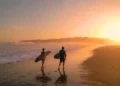 Surfers watch big breaking waves from beach after sunset surf session