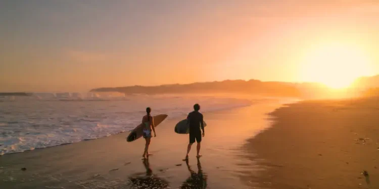 Surfers watch big breaking waves from beach after sunset surf session