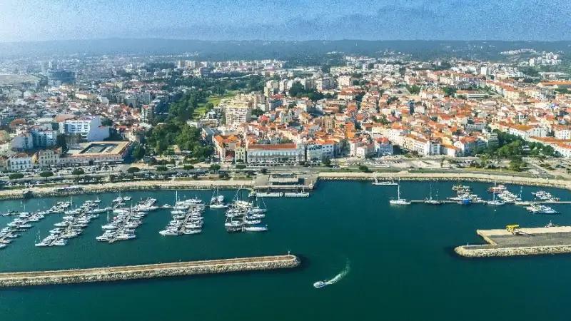 Aerial view of a coastal Portuguese city with red-tiled rooftops, a marina, and boats along the waterfront.