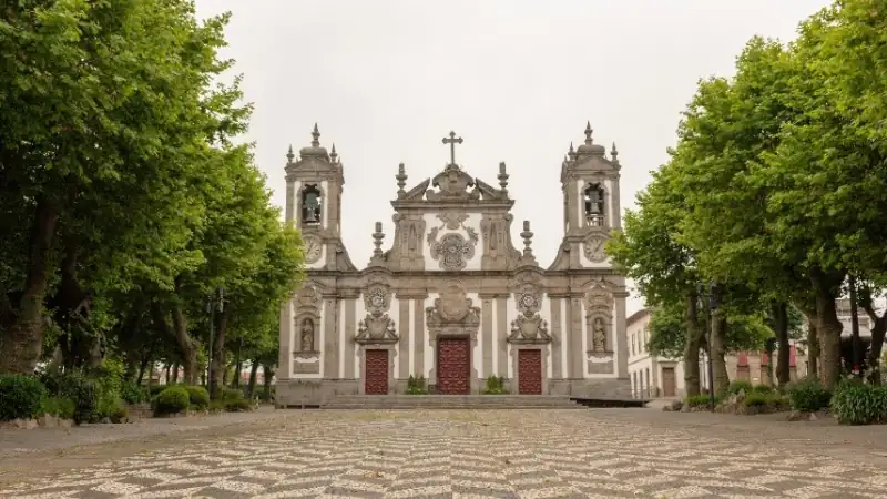 The Igreja Paroquial do Senhor Bom Jesus de Matosinhos, framed by lush trees and a traditional Portuguese cobblestone square.
