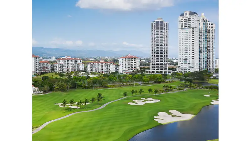 Luxury apartment balcony with modern outdoor lounge furniture, panoramic city skyline views, and lush green golf course surroundings.