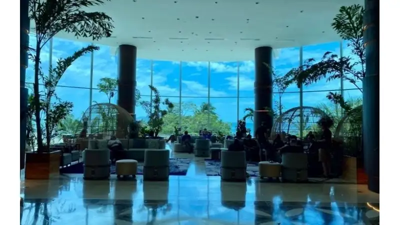 An elegant resort lobby with floor-to-ceiling windows overlooking tropical greenery and the ocean.