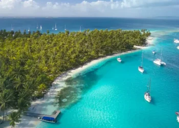 San Blas Islands, Panama - Drone Aerial View of many Sailboats & Sailing Yachts anchored in turquoise Water of Blue Lagoon next to white Sand Beach of Tropical Caribbean Island with green Palm Trees.