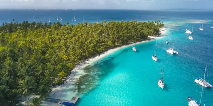 San Blas Islands, Panama - Drone Aerial View of many Sailboats & Sailing Yachts anchored in turquoise Water of Blue Lagoon next to white Sand Beach of Tropical Caribbean Island with green Palm Trees.