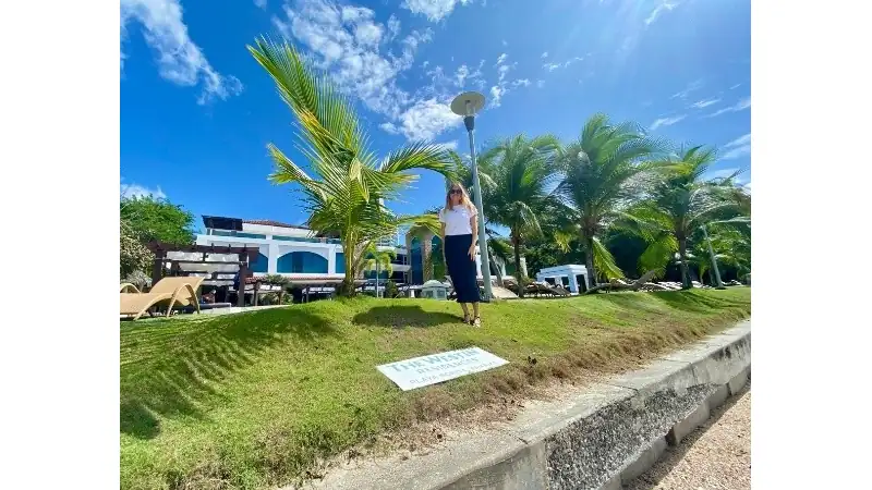 A woman stands on a grassy lawn surrounded by palm trees at a tropical resort.