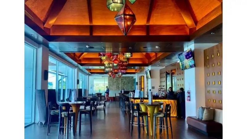 A resort bar and lounge featuring wooden ceilings, colorful pendant lights, and comfortable seating.