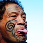 A tattoed Maori man sticking out his tongue