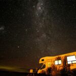 A camper parked under the night sky filled with stars