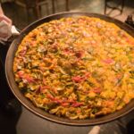 A waitress holds out a huge pan of paella.