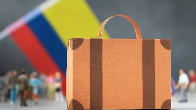 Cardboard suitcase, plastic toy people and the Colombian flag on an abstract background